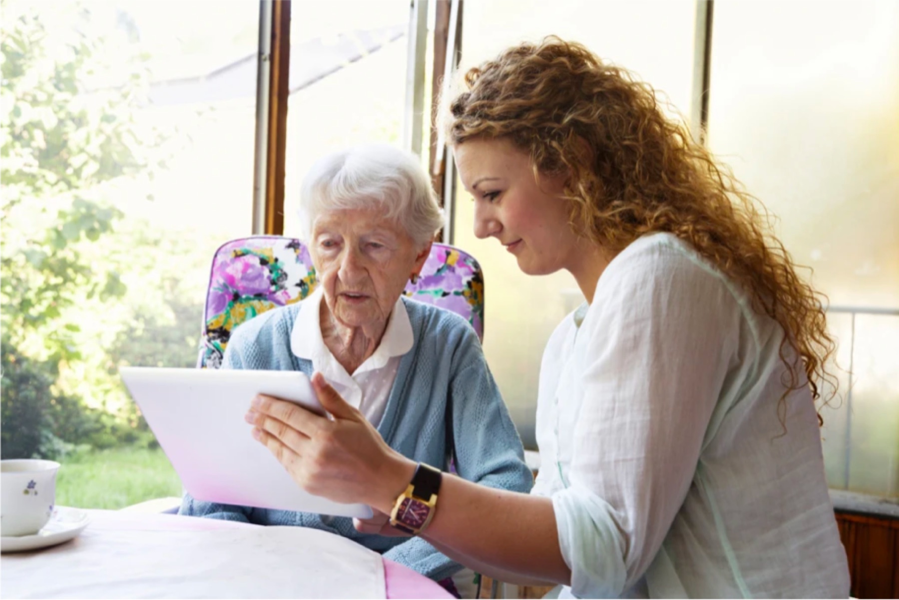 A carer and an older woman using a tablet together at a table