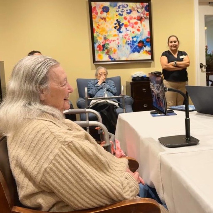 A resident laughing during a MentiaCompanion session, with care staff nearby